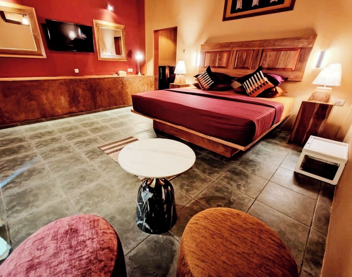 Ett hotellrum med en säng, ett litet runt bord, en soffa och en tv som är monterad på väggen.
