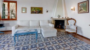 Sala de estar com sofá branco, mesa de centro azul, ladrilhos estampados, lareira e obras de arte penduradas na parede.