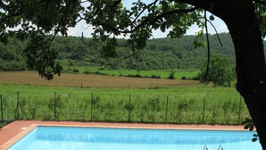 Piscina com duas espreguiçadeiras e vista para uma paisagem verde.