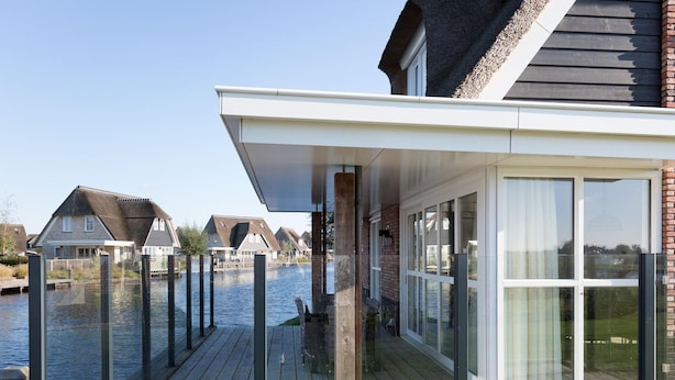 A modern house with a deck overlooking a canal, featuring large windows and a brick facade. - Beautiful Villa With Wellness (Delfstrahuizen)