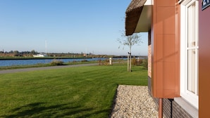 A building with a number 21 sign, a grassy lawn, a pathway, and a body of water in the background. - Beautiful Villa With Wellness (Delfstrahuizen)
