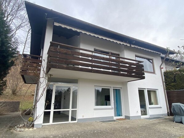 A two-story house with a balcony, large windows, and a door.