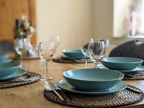 A dining table set with teal plates and clear wine glasses, accompanied by cutlery on woven placemats. - Old Forge Modern Retreat (Drebach)