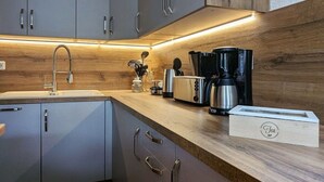 Une cuisine moderne avec des meubles gris, un plan de travail en bois, une machine à café, un grille-pain et une boîte à thé.