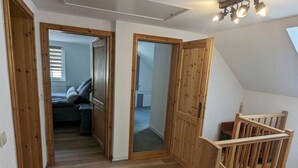 Un couloir au plancher de bois menant à une chambre à coucher équipée d’un lit et d’une fenêtre.