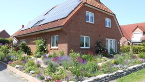 Een tweelaags bakstenen huis met zonnepanelen op het dak en een tuin met verschillende bloemen en planten.