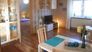 Een gezellige woonkamer met een televisie, houten kasten en een eethoek met een tafel en stoelen.