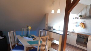 Een compacte keuken met een eethoek, houten stoelen, een witte tafel en een zichtbare oven.