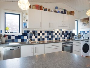 A modern kitchen with white cabinets, a granite countertop, a built-in dishwasher, and a washing machine. - 4 Star Holiday Home in Bovallstrand (Bovallstrand)