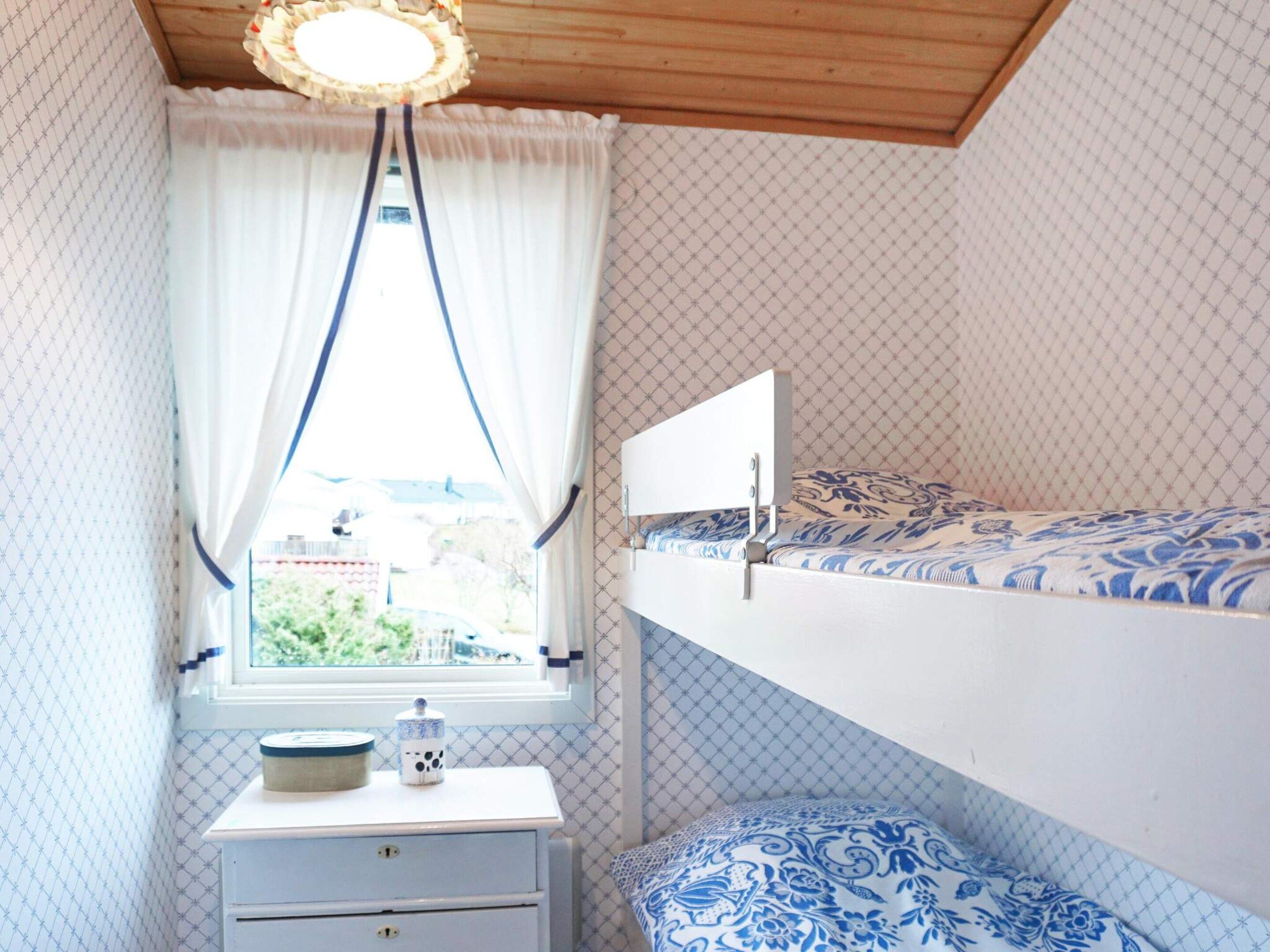 Un dormitorio con una litera, una mesita de noche con lámpara y una ventana con cortinas.