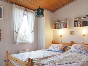 Une chambre à coucher avec un lit en bois, une fenêtre avec des rideaux, une bibliothèque et une lampe fixée au mur.