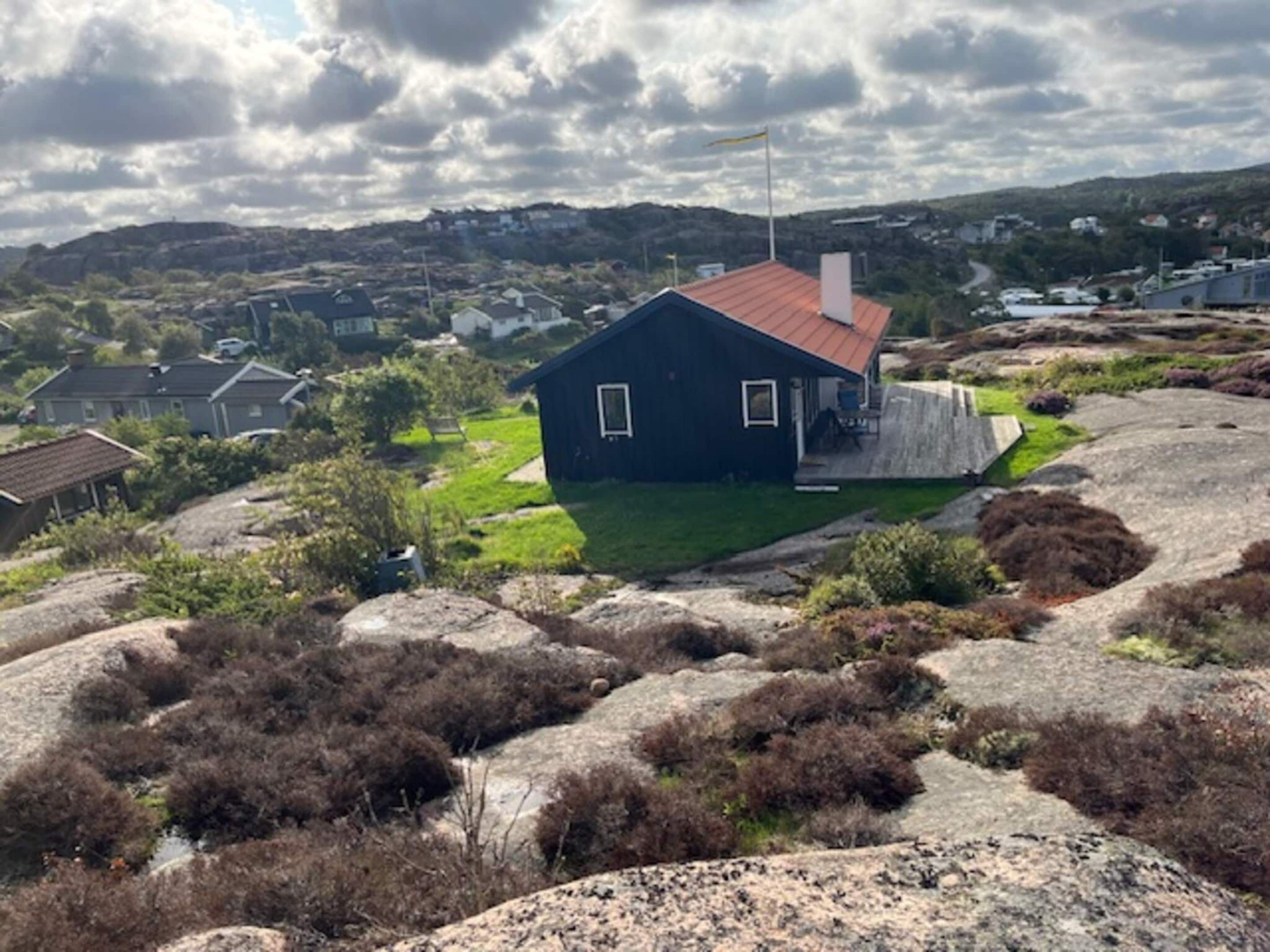 A small, dark blue house with a red roof, surrounded by rocky terrain and sparse vegetation.