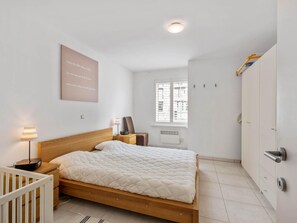 Un dormitorio con una cama de madera, una lámpara de noche, una silla, un radiador y un armario.