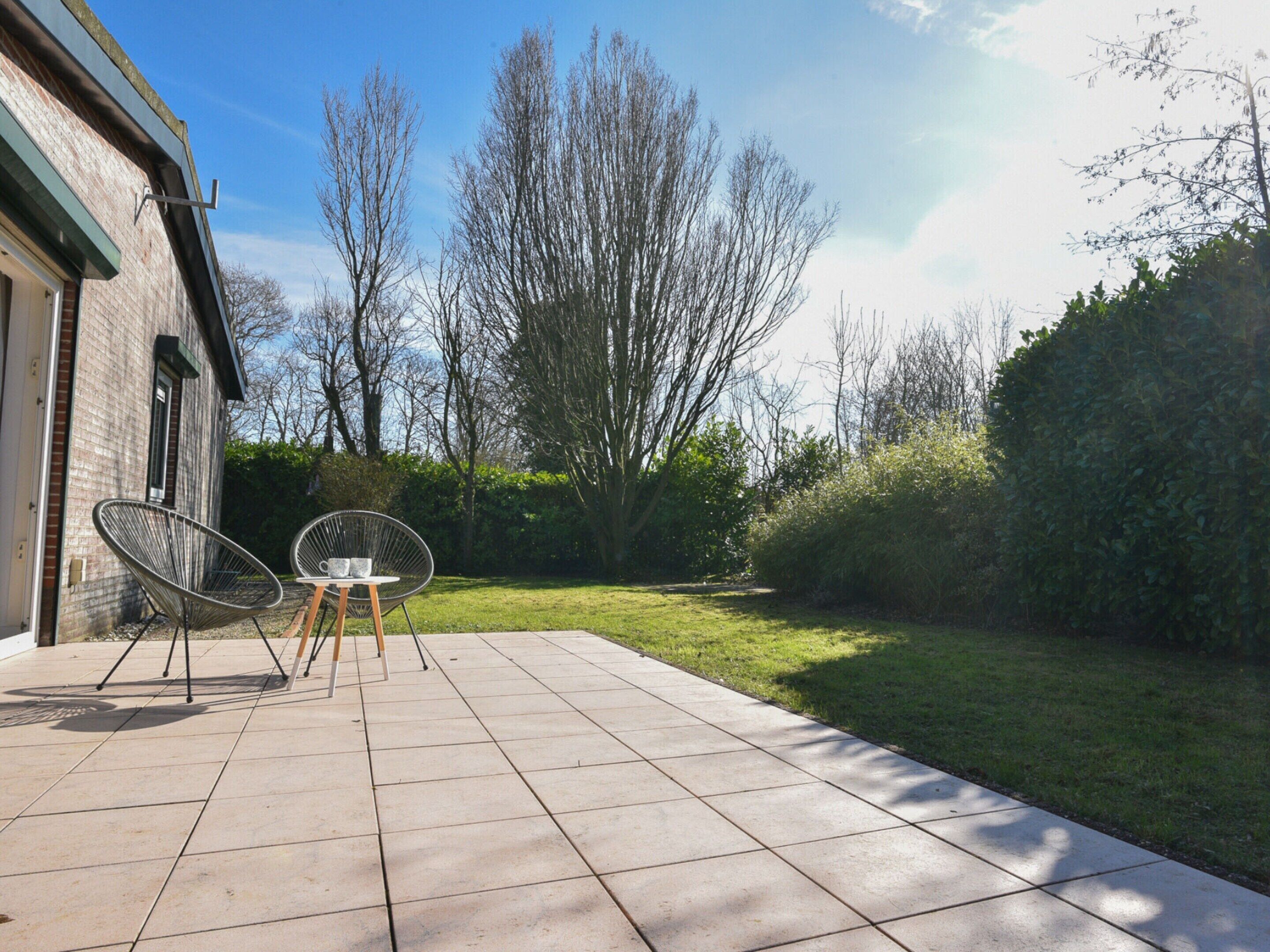 A patio with two chairs and a table, a brick building, and a grassy area with trees.
