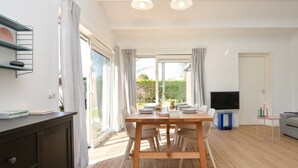 A bright, well-lit room with a wooden dining table set for four, a television, and a sofa. - Your Coastal Hideaway (Kamperland)