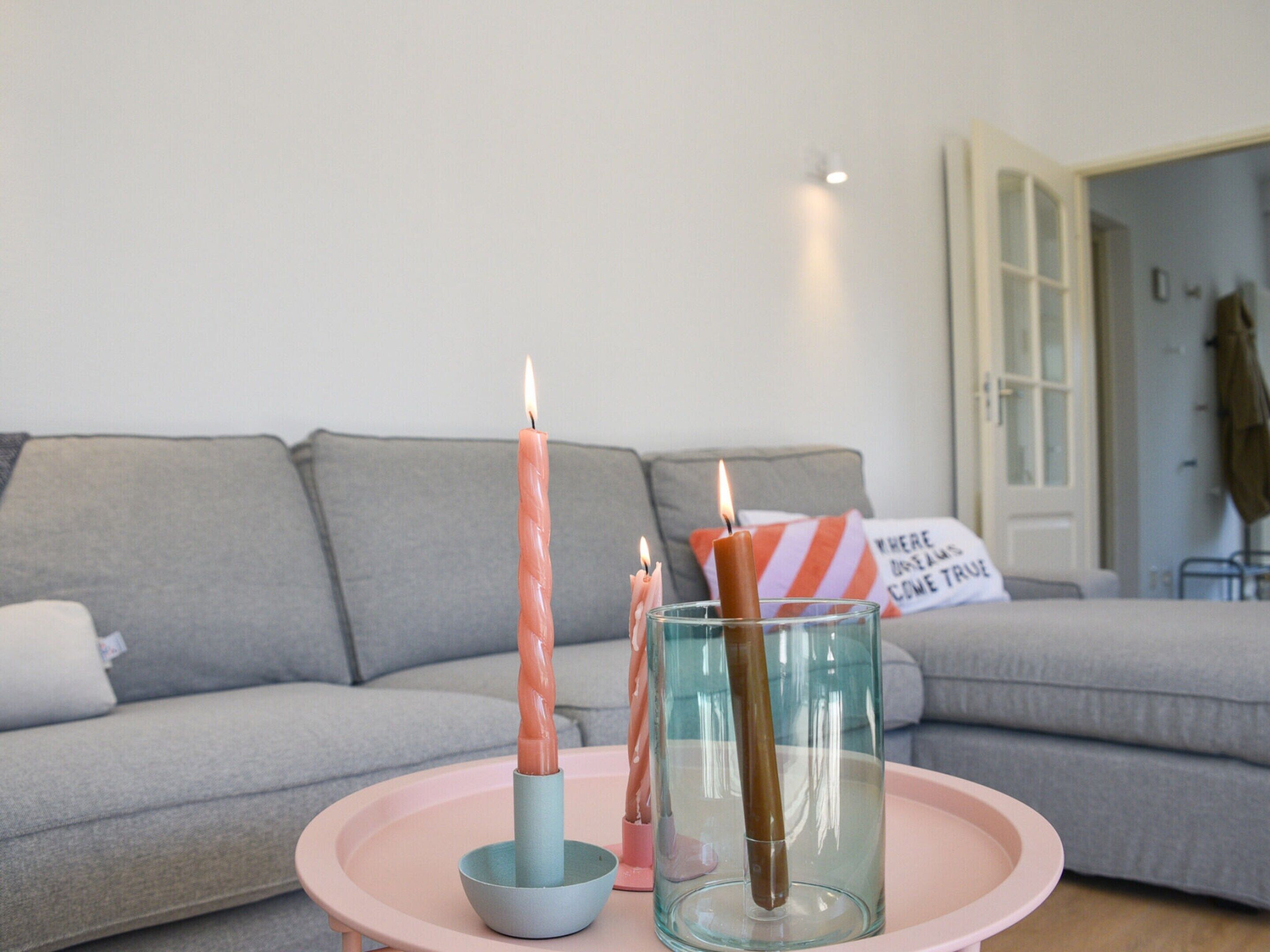Un salon avec un canapé gris, un plateau rose orné de bougies et un vase en verre.