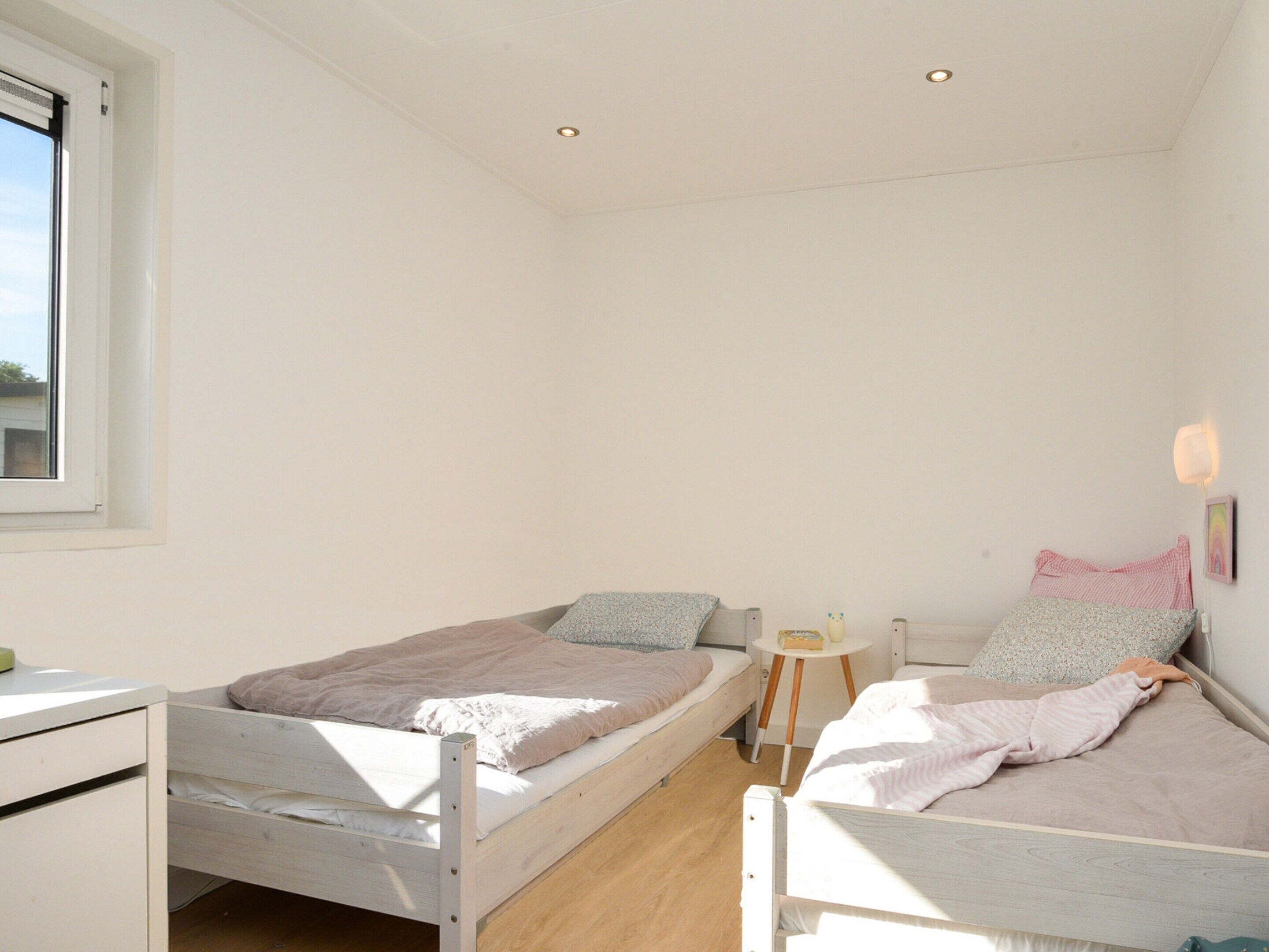 Une petite chambre bien éclairée, avec deux lits simples, une petite table de chevet et une fenêtre.