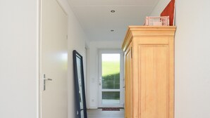 A hallway with a wooden cabinet, a door, and a glass door leading to a room. - Your Coastal Hideaway (Kamperland)