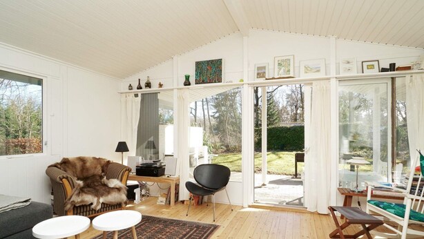 A cozy living room with a sofa, a chair, a small table, and a rug. There is a glass door leading to an outdoor area with a bench and a table. - 5 Person Holiday Home in Melby (Melby)
