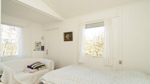 A room with a large bed, a smaller bed, and a chair. There is a window with curtains, a door, and a wall-mounted light fixture. - 5 Person Holiday Home in Melby (Melby)