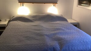En säng med ett mönstrat överkast, två sänglampor, en inramad tavla ovanför sängen och ett litet nattduksbord med en lampa.