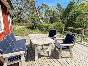 A wooden deck with a table and four chairs, surrounded by greenery and trees. - 4 Star Holiday Home in Torhamn (Torhamn)