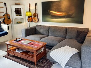 A living room with a grey sofa, a wooden coffee table, a lamp, and two guitars. - 4 Star Holiday Home in Torhamn (Torhamn)