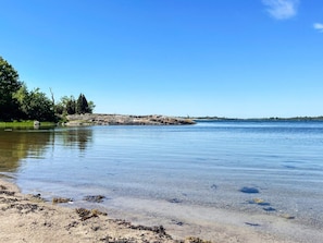 A calm lake with a sandy shore and a rocky outcrop in the distance. - 4 Star Holiday Home in Torhamn (Torhamn)