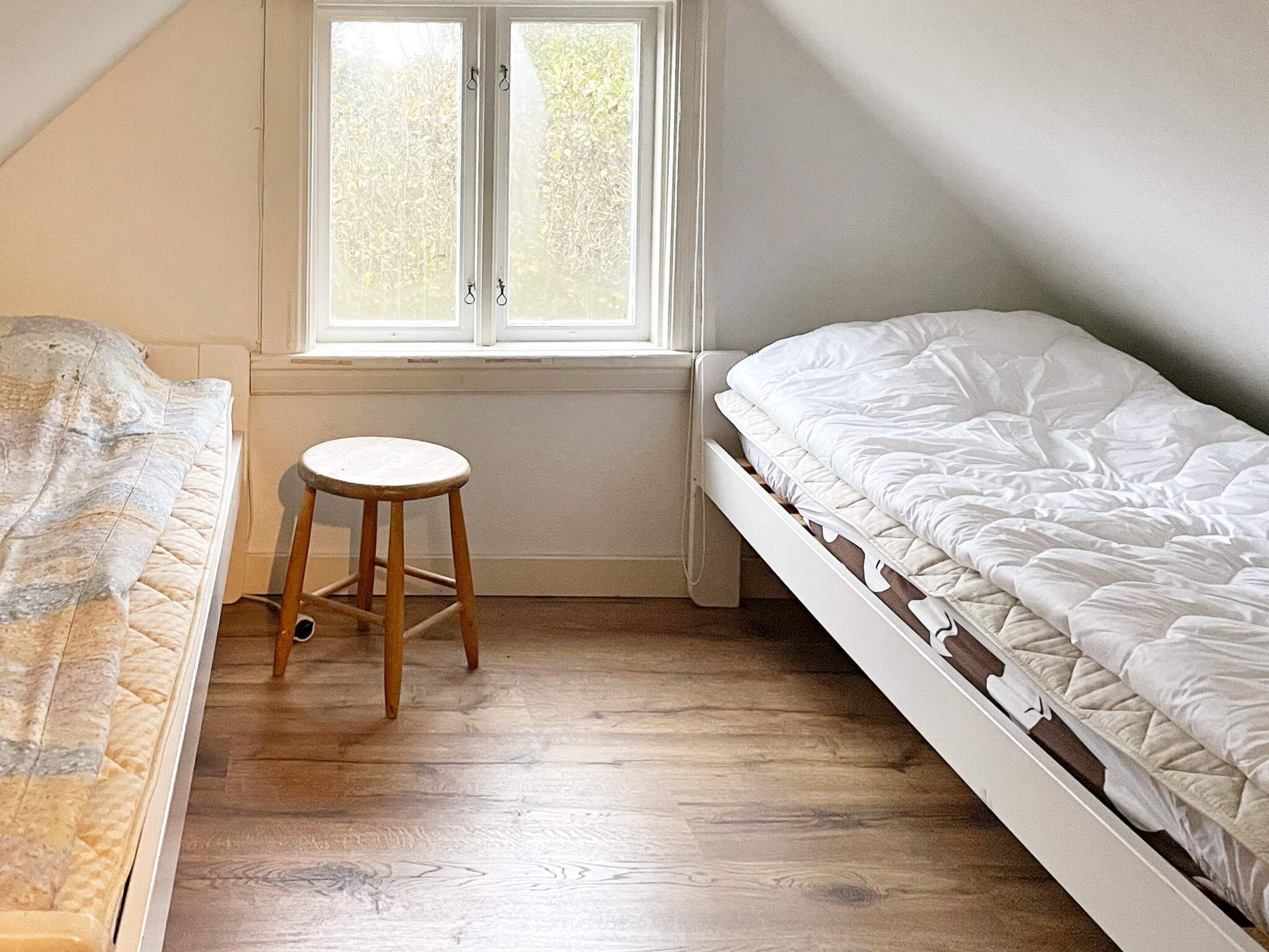 Un dormitorio con piso de madera, una ventana con contraventanas blancas y dos camas.