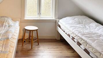 Un dormitorio con piso de madera, una ventana con contraventanas blancas y dos camas.
