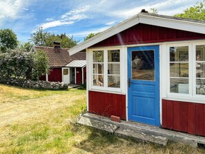 A red and white building with a blue door, a stone wall, and a grassy area. - 4 Star Holiday Home in Torhamn (Torhamn)