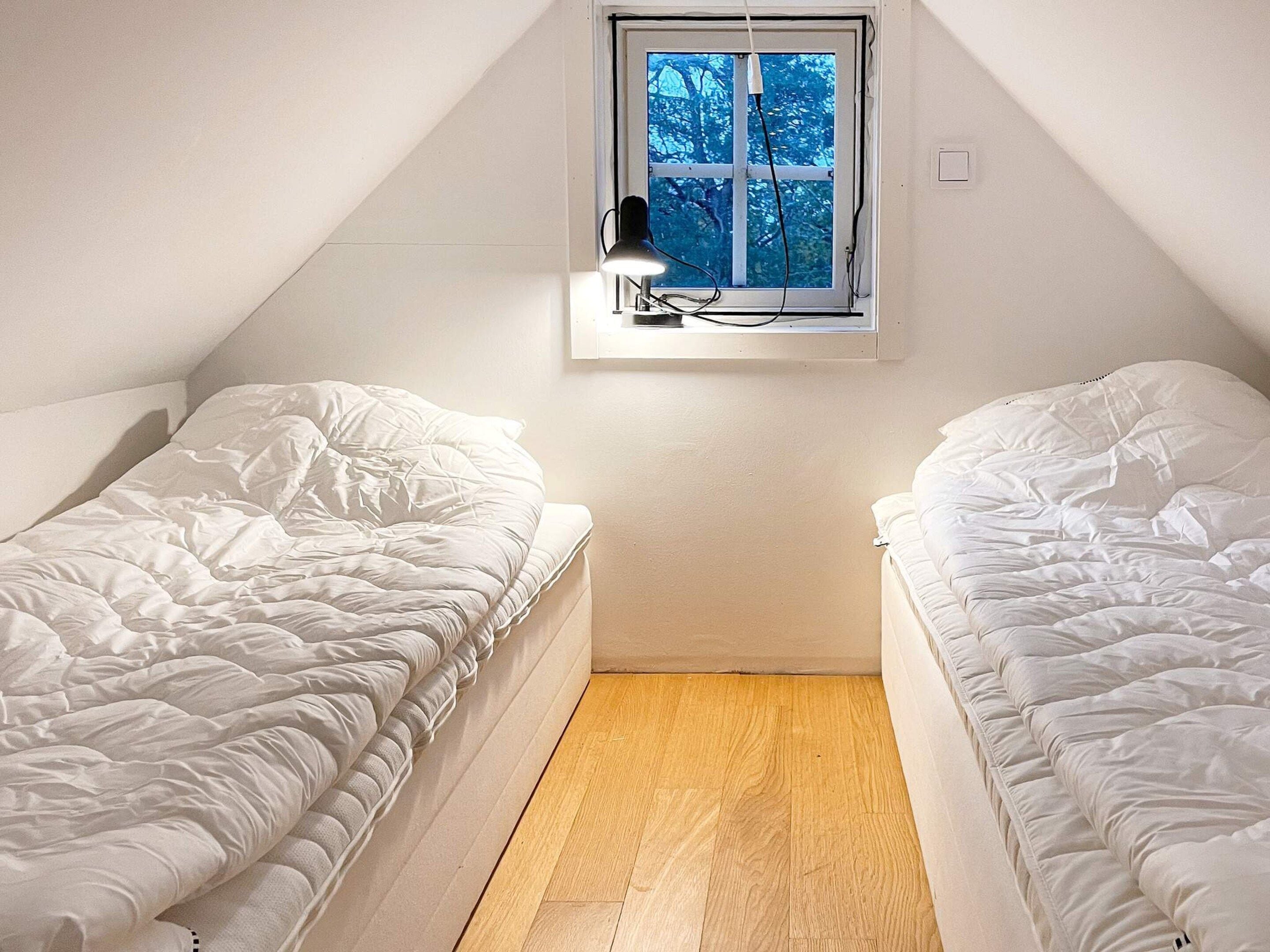 A small, single-room with two beds, a window with a view of trees, and a wooden floor.