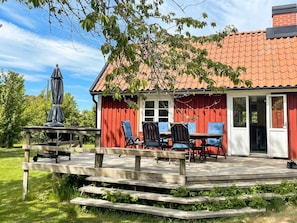 A wooden deck with a table and chairs, a covered outdoor seating area, and a red building with a tiled roof. - 4 Star Holiday Home in Torhamn (Torhamn)