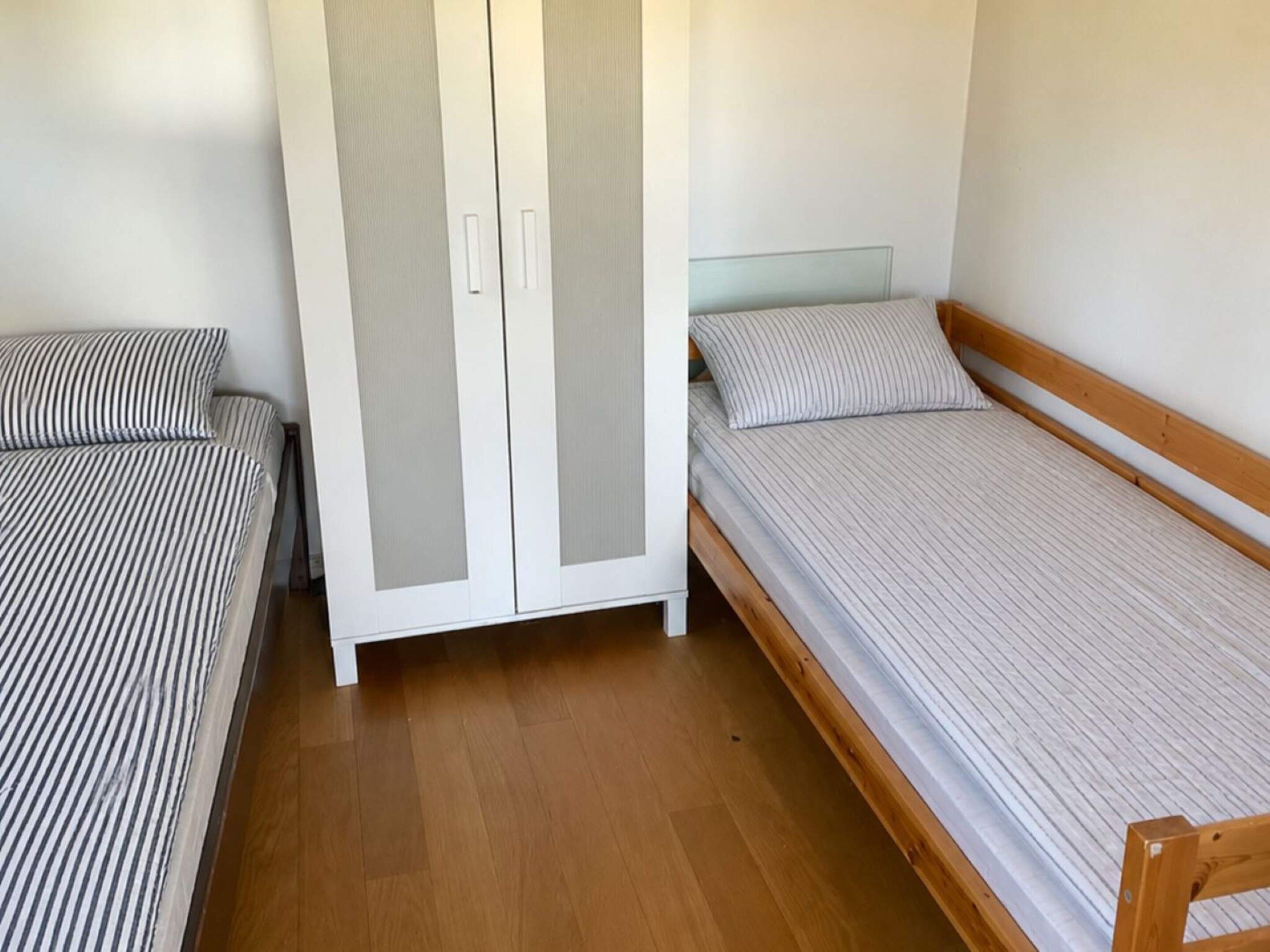 A bedroom with two single beds, a wardrobe, and a wooden floor.