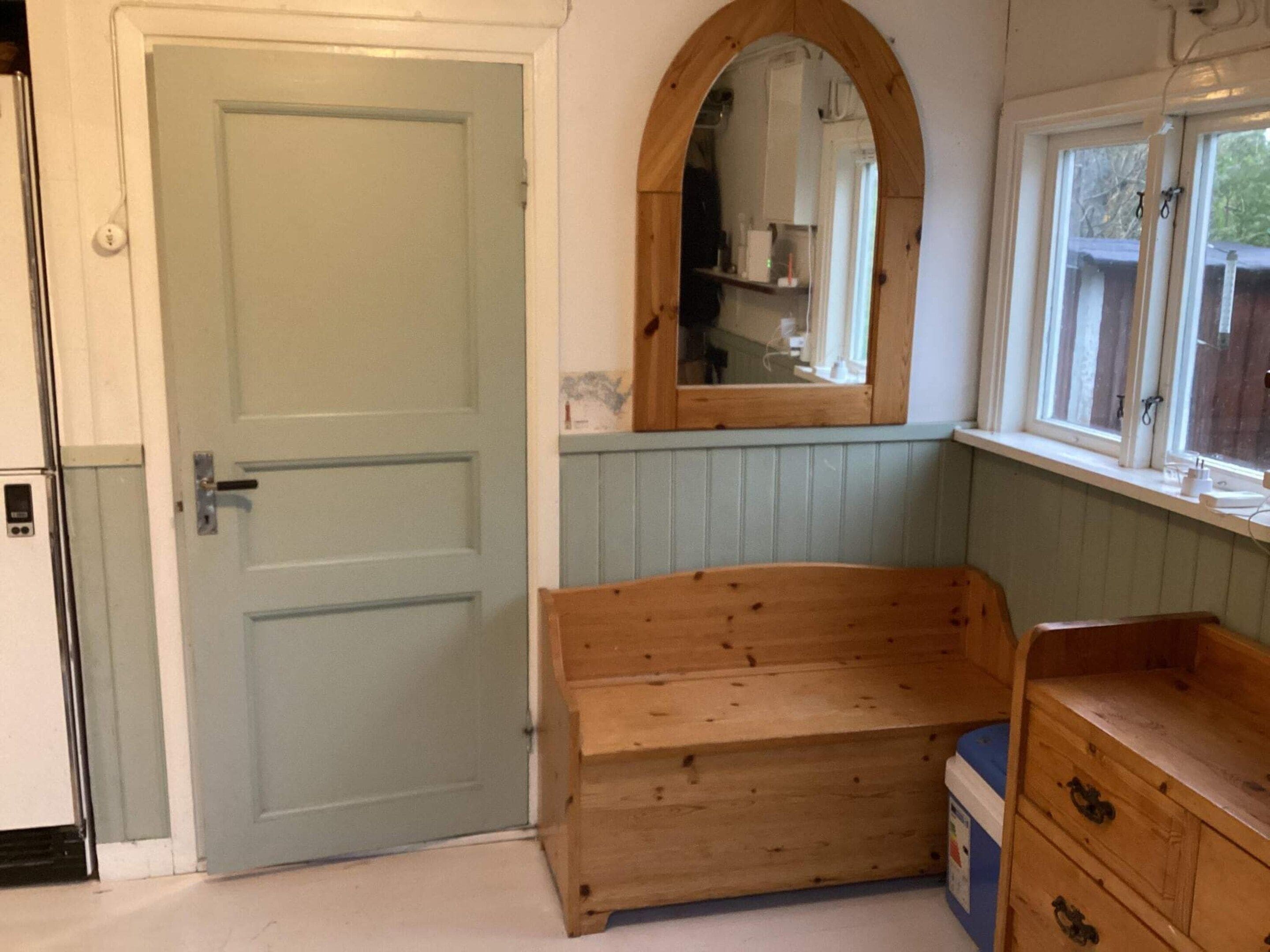 A room with a closed door, a wooden bench, a dresser, and a window with a view.