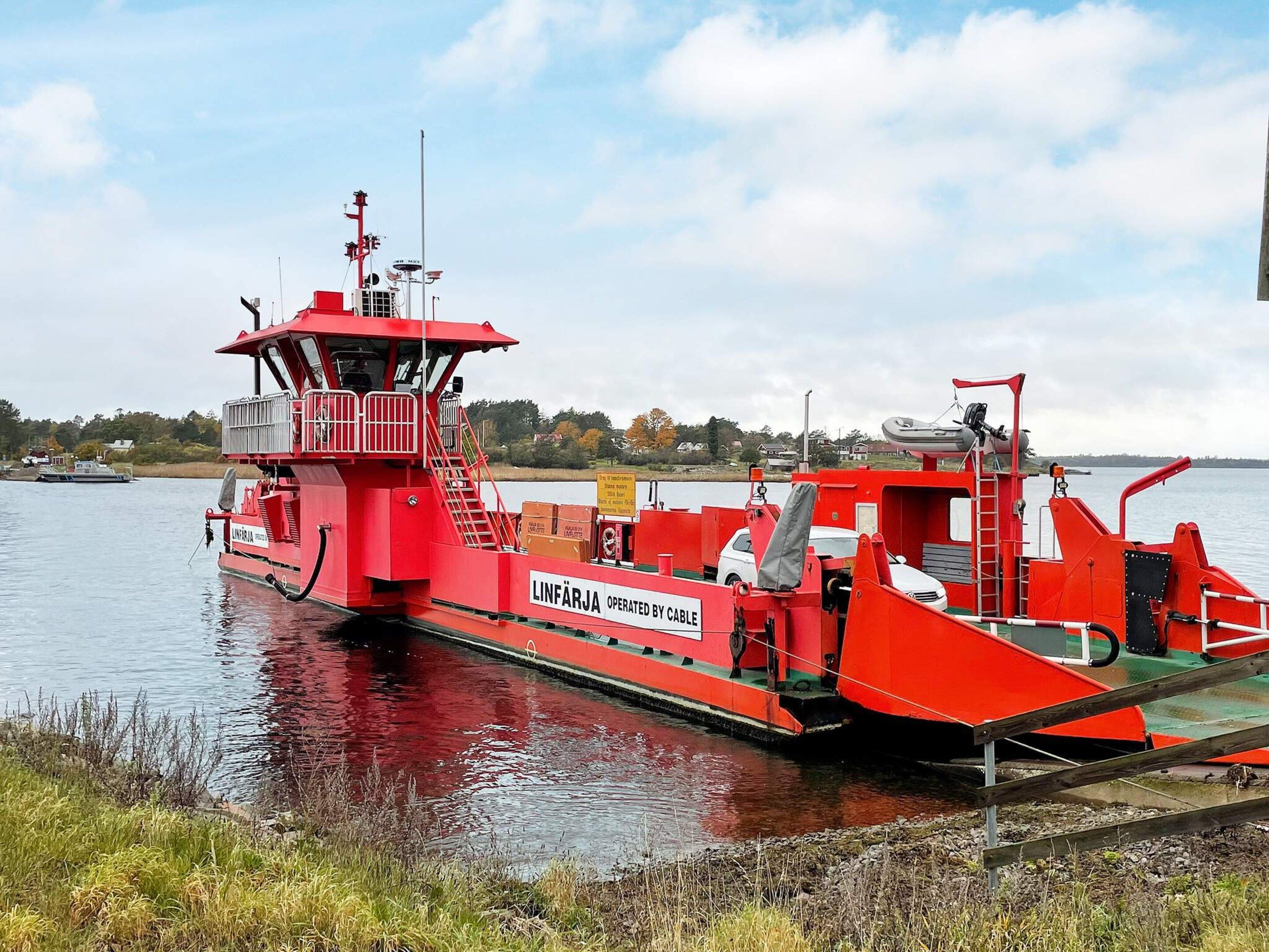 A red ferry with a cabin and ramp, docked at a pier.
