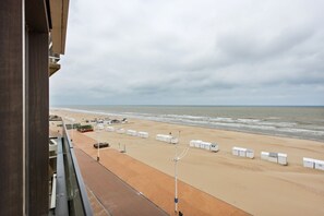 A beach view from a balcony with a sandy beach, white beach huts, and a cloudy sky.