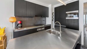 Una cocina moderna con armarios oscuros, encimeras de acero inoxidable, horno integrado y cafetera.
