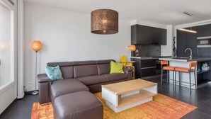 Una sala de estar moderna con un sofá seccional, una mesa de centro de madera y una cocina con armarios oscuros y un taburete de bar.