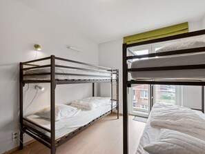 A dormitory room with bunk beds, a window with a view of buildings, and a wall-mounted light.