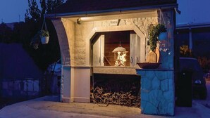 A stone-built outdoor pizza oven with a fire burning inside, surrounded by a rustic stone structure. - Apartment Niko - Two Bedroom Apartment With Swimming Pool (Sibenik)