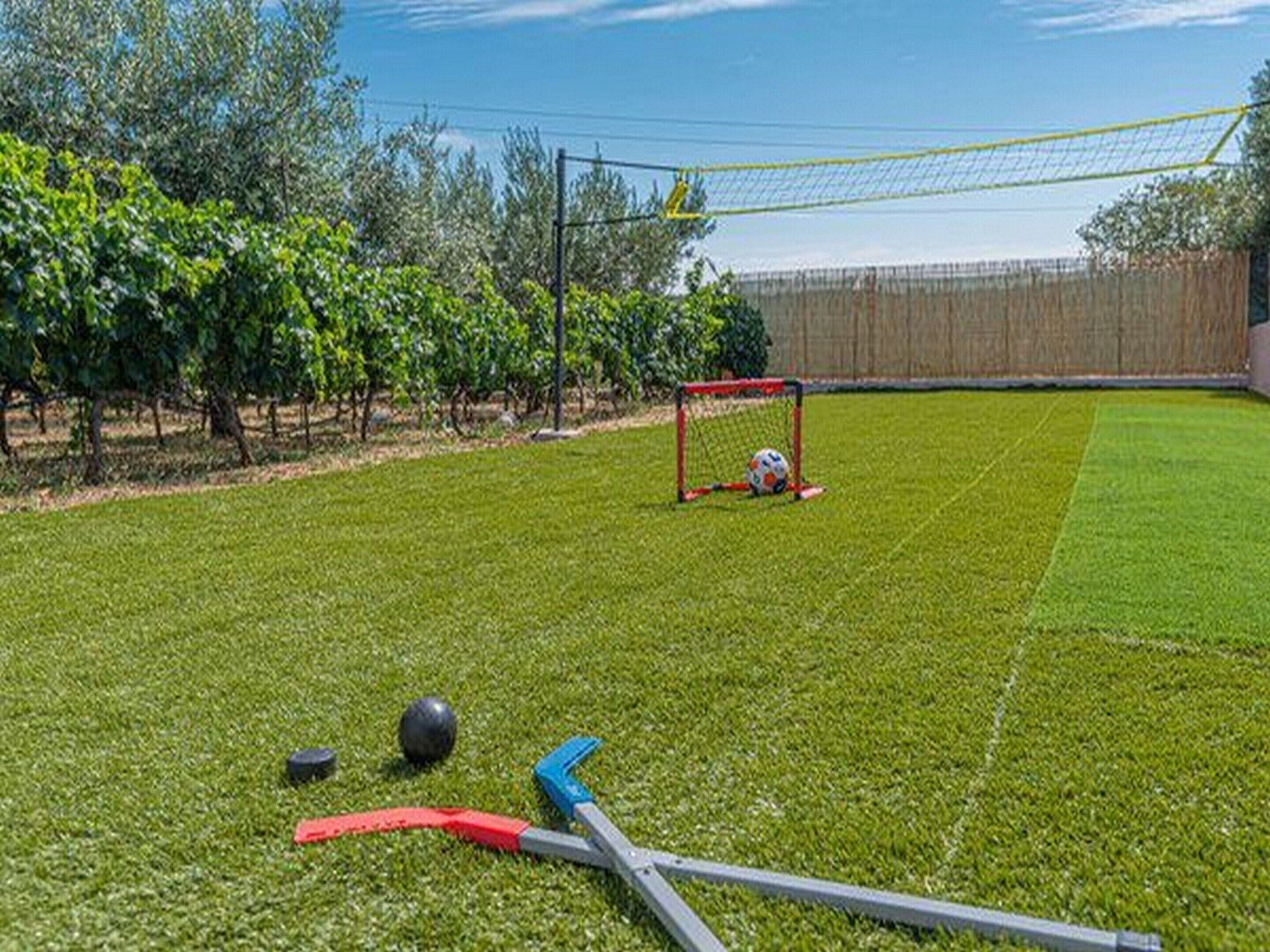A grassy outdoor area with a goalpost, a soccer ball, and two hockey sticks.