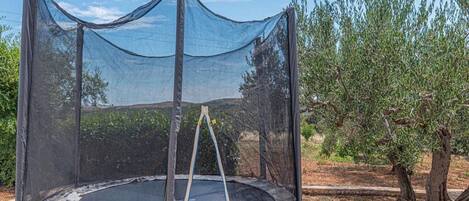 A trampoline with a safety net, surrounded by trees and a clear sky.
