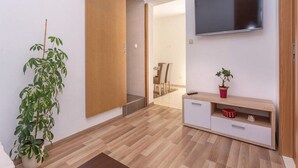 A modern living room with a sliding wooden door, a mounted TV, a wooden cabinet with drawers, and a potted plant. - Apartment Niko - Two Bedroom Apartment With Swimming Pool (Sibenik)