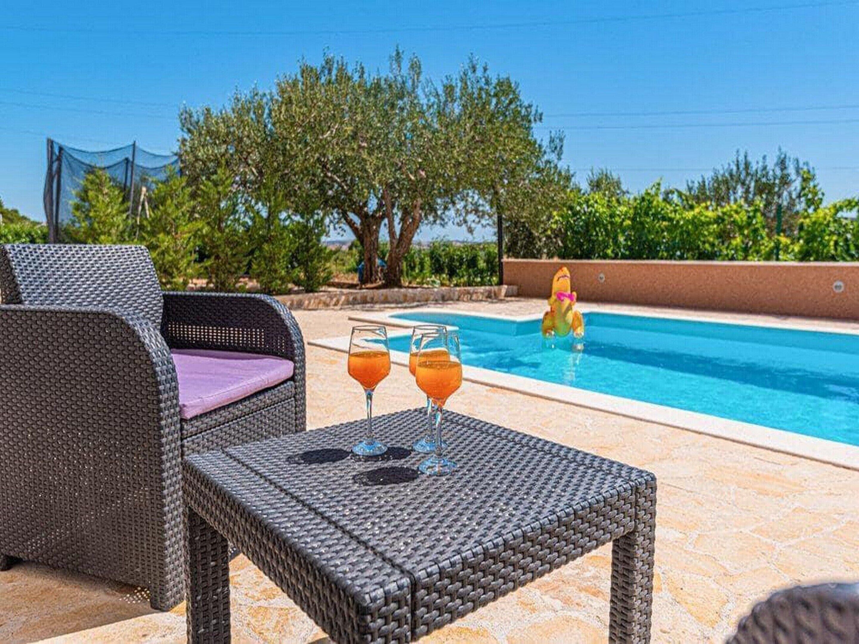 A poolside area with wicker furniture and two glasses of orange beverage on a table.