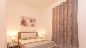 A bedroom with a bed, two bedside tables with lamps, a wall-mounted artwork, and a patterned curtain. - Apartment Niko - Two Bedroom Apartment With Swimming Pool (Sibenik)