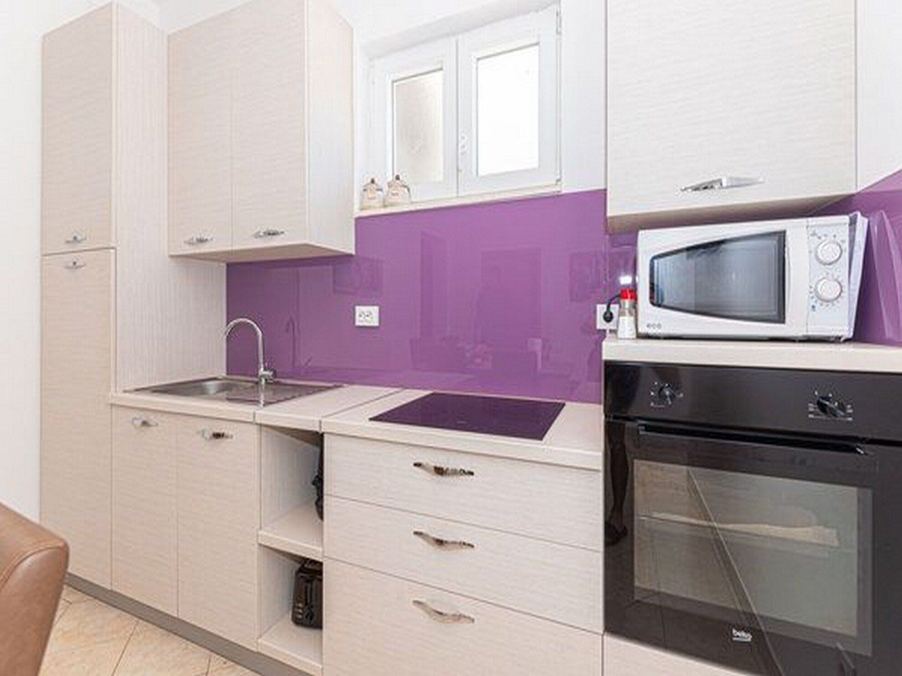 A compact kitchen with white cabinets, a sink, a microwave, and an oven.