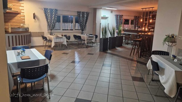 A spacious dining area with multiple tables and chairs, a bar area with stools, and a kitchen visible in the background. - Erbacher Hof  (Homburg)