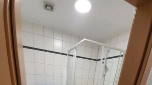 A bathroom with white tiled walls, a glass-enclosed shower, a toilet, and a blue towel rack. - Erbacher Hof  (Homburg)