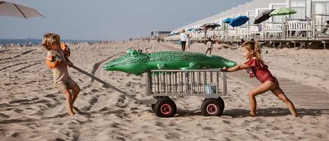 Escena de playa con un cocodrilo inflable verde que dos niños jalan.